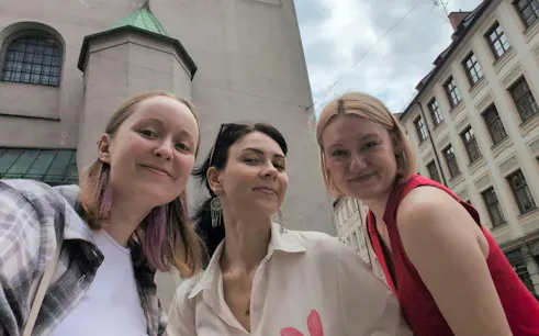Three people smiling in front of historic buildings in Munich during a city exploration game.