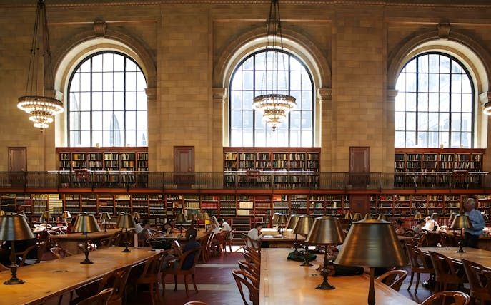 Interior reading room of the New York Public Library Stephen A. Schwarzman Building with large windows and chandeliers.