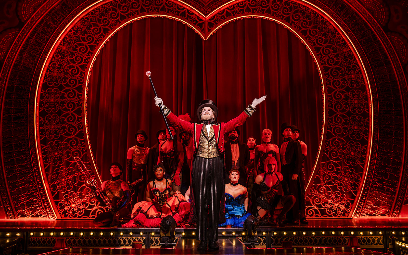 Performer in red coat leading ensemble on Moulin Rouge! The Musical stage, West End.