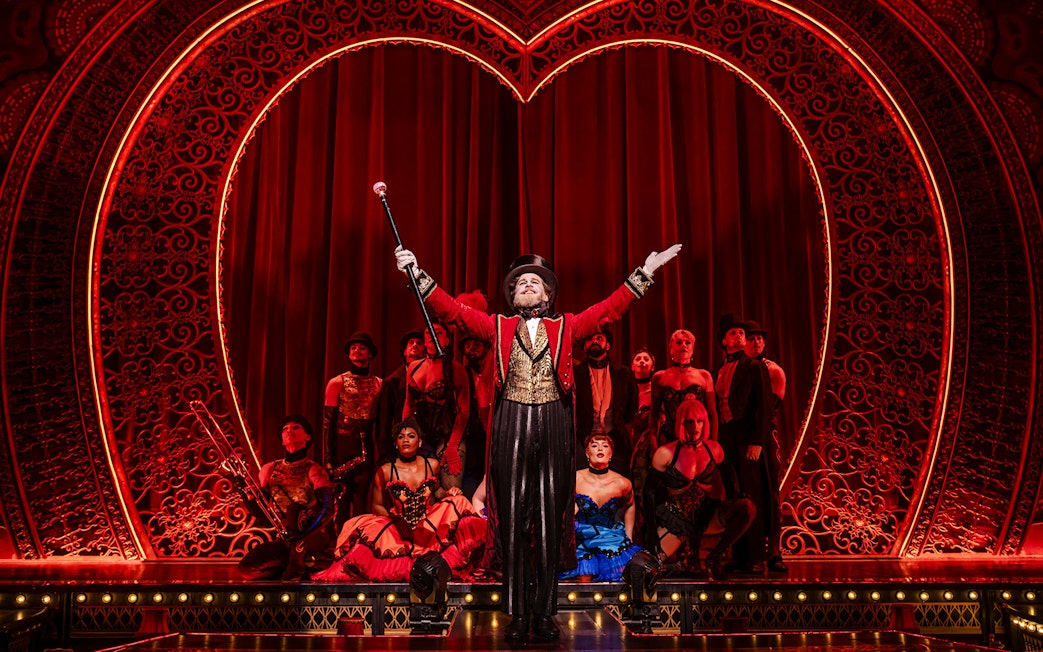 Performer in red coat leading ensemble on Moulin Rouge! The Musical stage, West End.