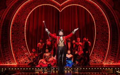 Performer in red coat leading ensemble on Moulin Rouge! The Musical stage, West End.