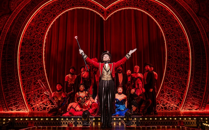 Performer in red coat leading ensemble on Moulin Rouge! The Musical stage, West End.