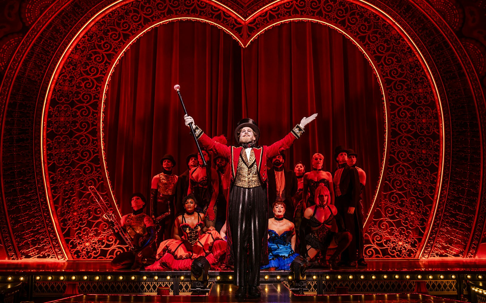 Performer in red coat leading ensemble on Moulin Rouge! The Musical stage, West End.