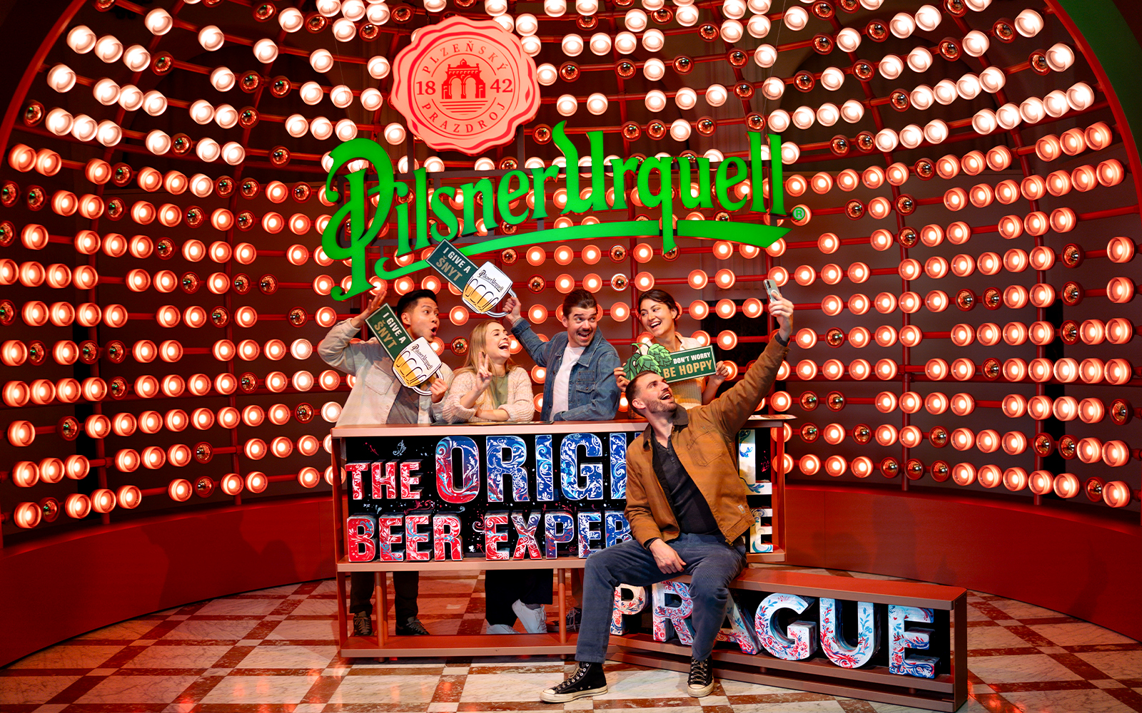 Group enjoying Prague Pilsner Urquell Experience with beer signs and lights.