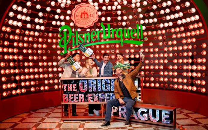 Group enjoying Prague Pilsner Urquell Experience with beer signs and lights.