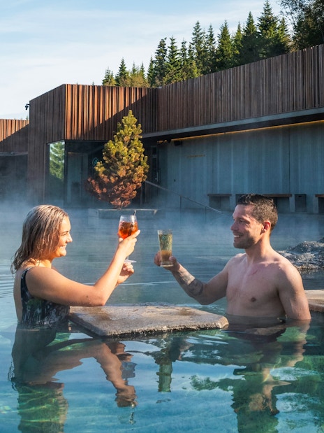 Couple enjoying drinks in Forest Lagoon geothermal spa, Vaðlaskógur forest, near Akureyri, North Iceland.