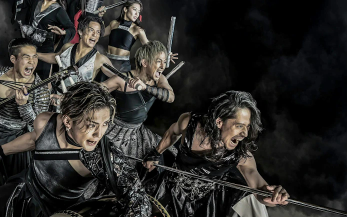 Performers in dynamic pose with drumsticks at DRUM TAO Theater, Kyoto.