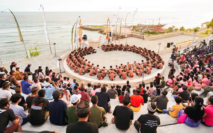Kecak dancers performing in a circle at Ubud amphitheater with ocean view.