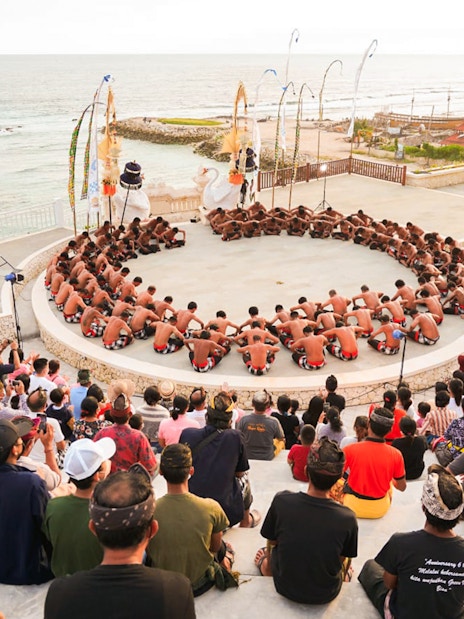 Kecak dancers performing in a circle at Ubud amphitheater with ocean view.