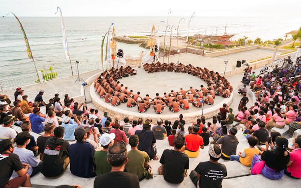 Kecak dancers performing in a circle at Ubud amphitheater with ocean view.