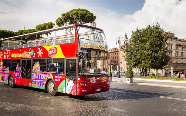 Open-top sightseeing bus in Rome near historical buildings.