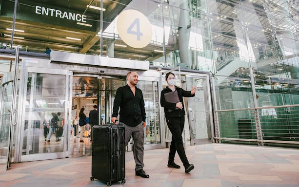 Man with luggage being greeted by a guide at Bangkok airport entrance for private transfer.