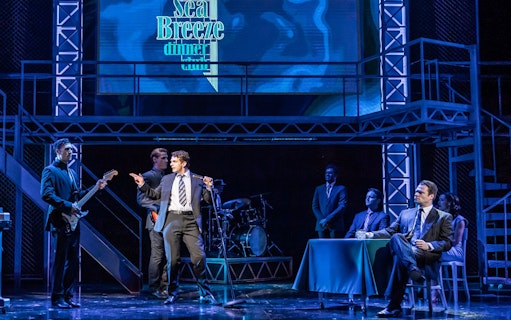 Stage performance of Jersey Boys with actors singing and playing instruments.