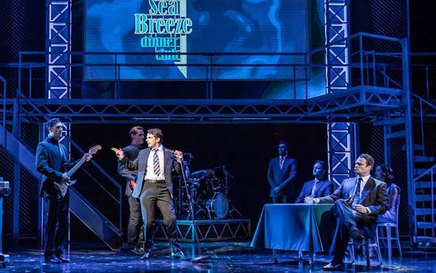 Stage performance of Jersey Boys with actors singing and playing instruments.
