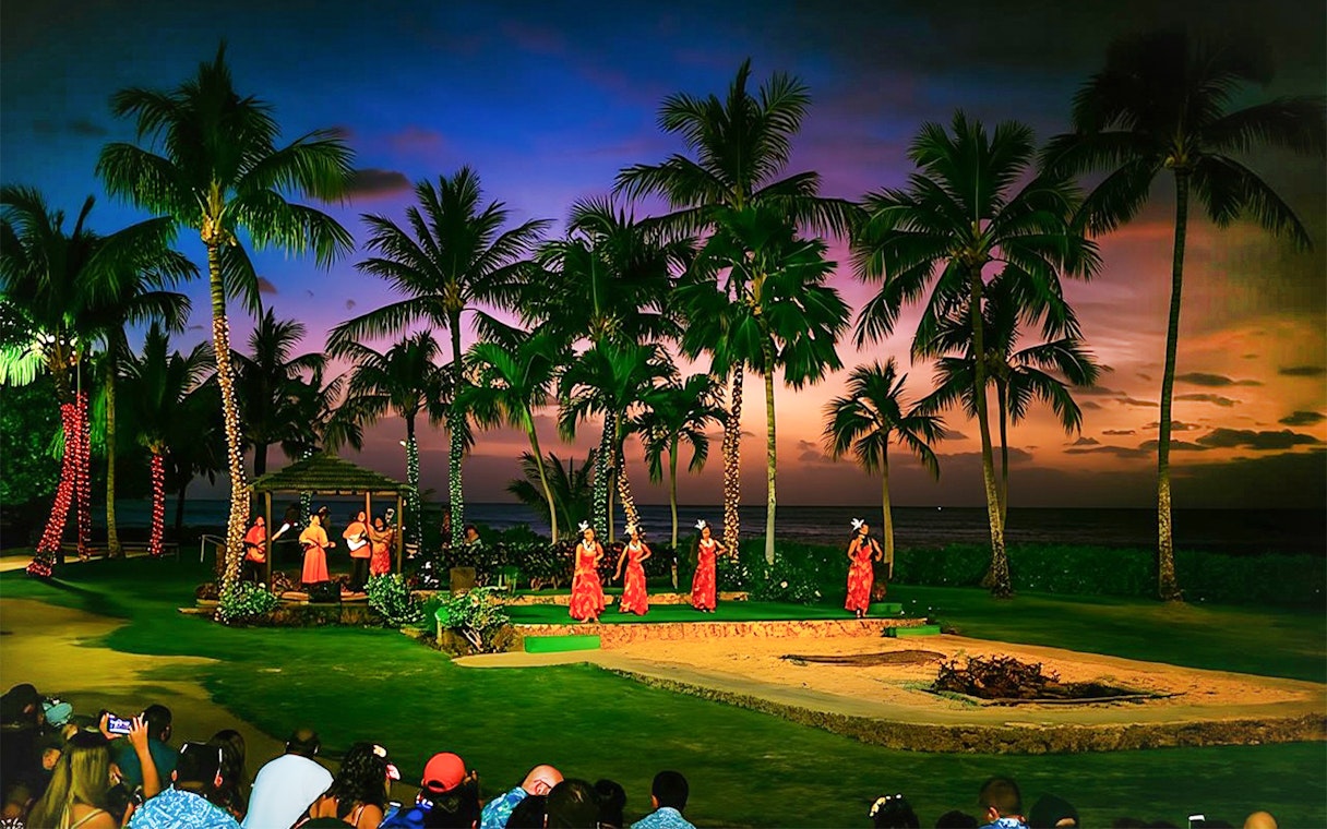 Dancers performing at Paradise Cove Luau, Hawaii, with palm trees and sunset in the background.