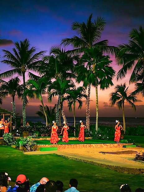 Dancers performing at Paradise Cove Luau, Hawaii, with palm trees and sunset in the background.