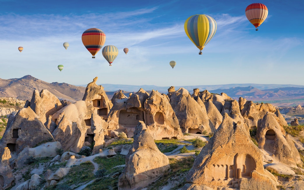 Cave dwellings and hot air balloons over rock formations in Cappadocia, Turkey.