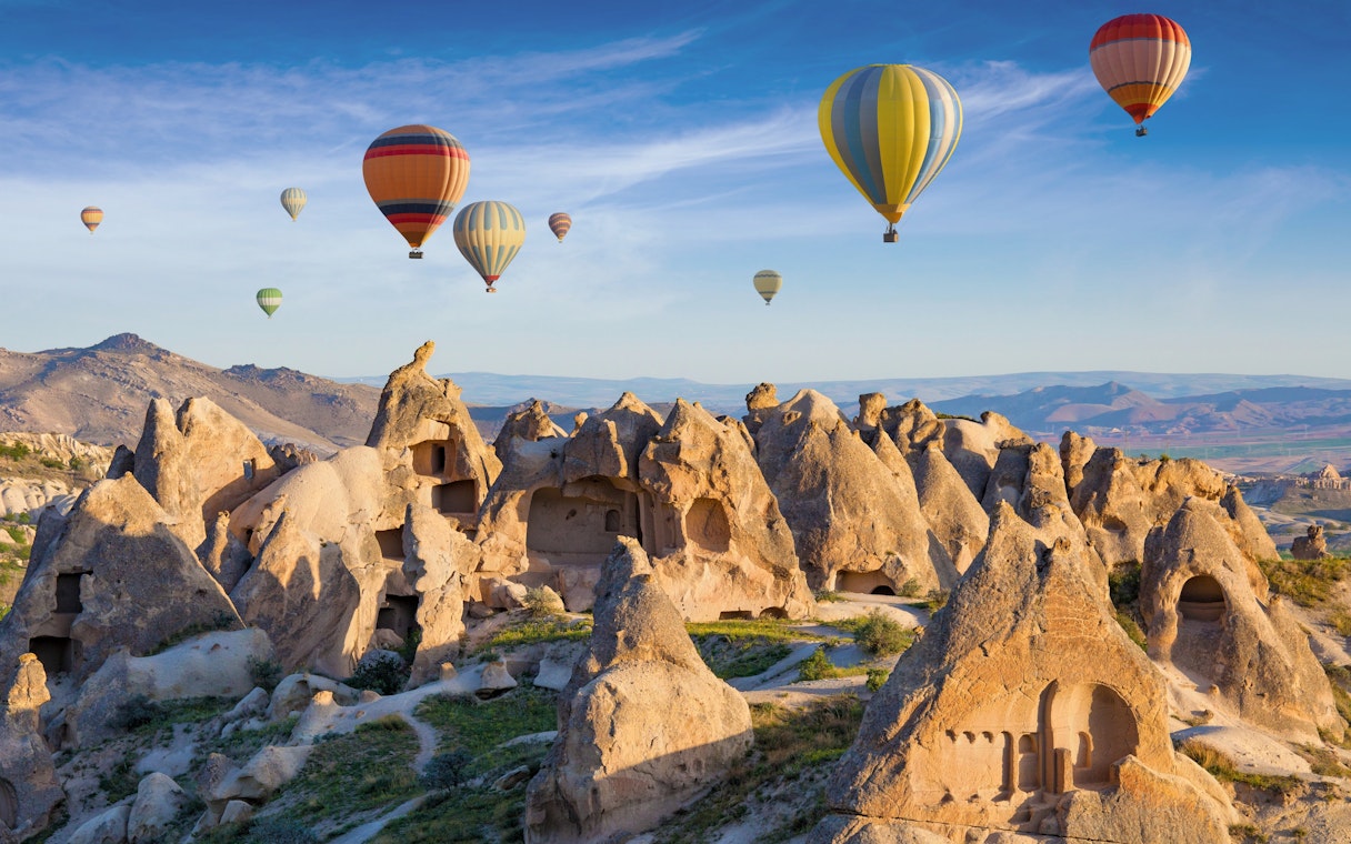 Cave dwellings and hot air balloons over rock formations in Cappadocia, Turkey.