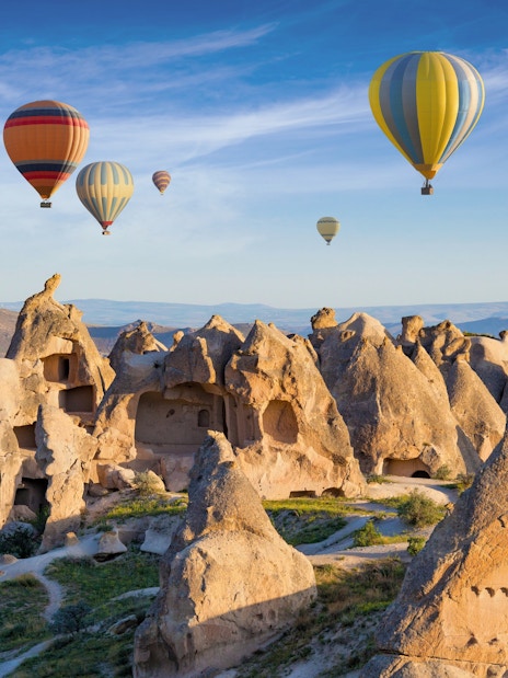 Cave dwellings and hot air balloons over rock formations in Cappadocia, Turkey.
