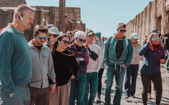Tour group with audio guides exploring Pompeii ruins.