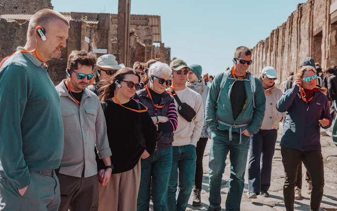 Tour group with audio guides exploring Pompeii ruins.