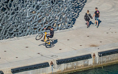 Cyclist performing a wheelie near Mucem's unique facade in Marseille.