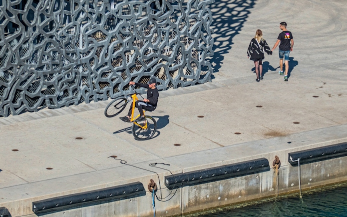 Cyclist performing a wheelie near Mucem's unique facade in Marseille.