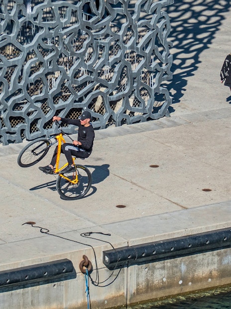 Cyclist performing a wheelie near Mucem's unique facade in Marseille.