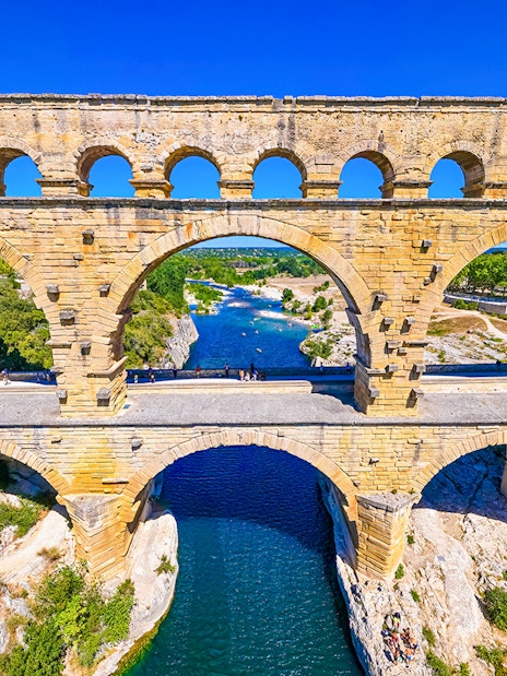 Pont du Gard aqueduct over river in Nîmes, France, with surrounding landscape.
