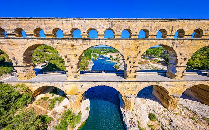 Pont du Gard aqueduct over river in Nîmes, France, with surrounding landscape.