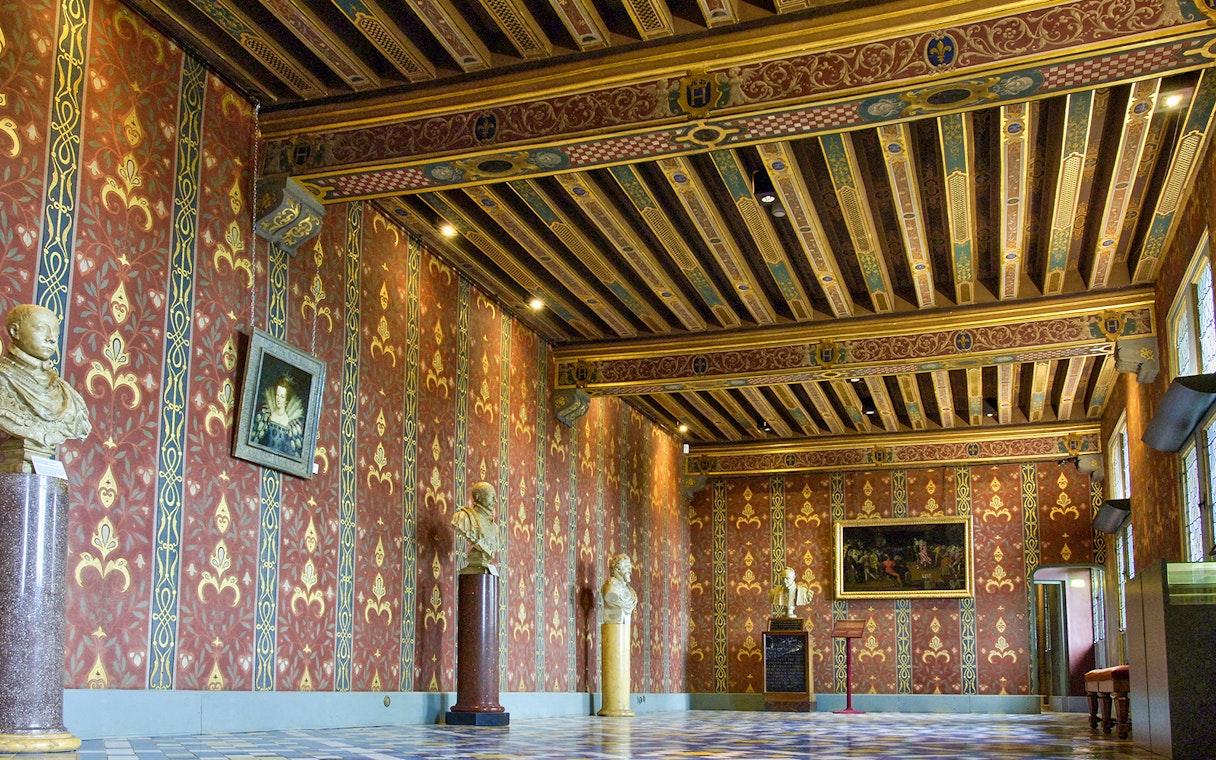 Interior of Royal Blois Castle with ornate red and gold walls, decorative ceiling, and sculptures.
