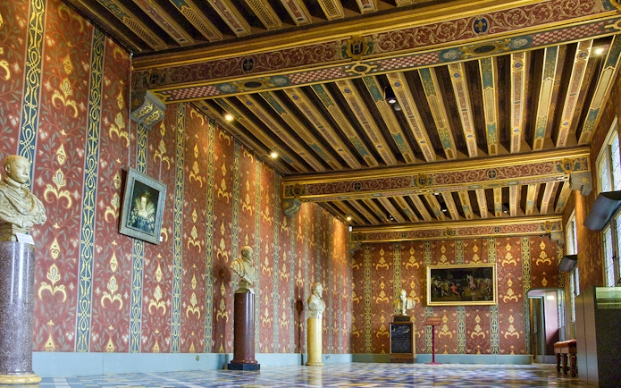 Interior of Royal Blois Castle with ornate red and gold walls, decorative ceiling, and sculptures.