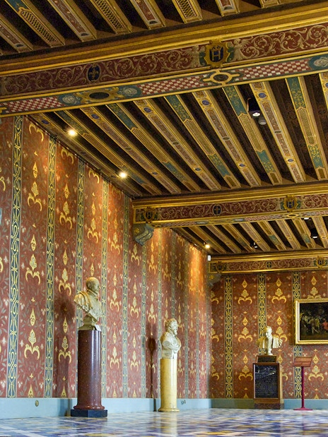 Interior of Royal Blois Castle with ornate red and gold walls, decorative ceiling, and sculptures.