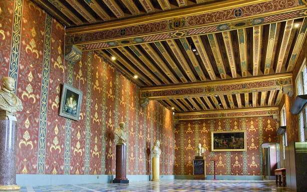 Interior of Royal Blois Castle with ornate red and gold walls, decorative ceiling, and sculptures.