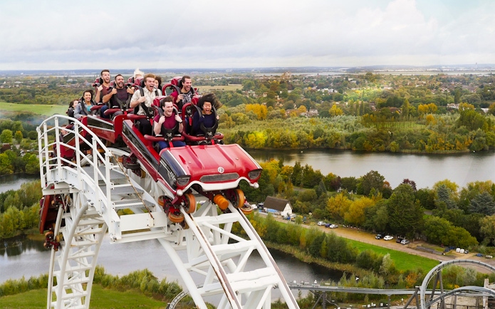 Roller coaster descending at Thorpe Park with riders enjoying the view of surrounding landscape.