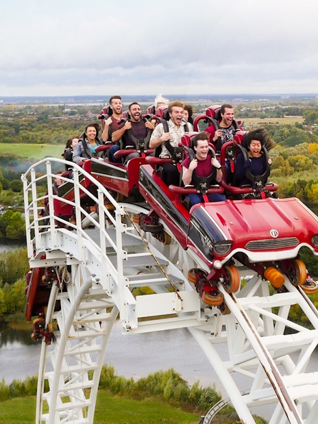 Roller coaster descending at Thorpe Park with riders enjoying the view of surrounding landscape.