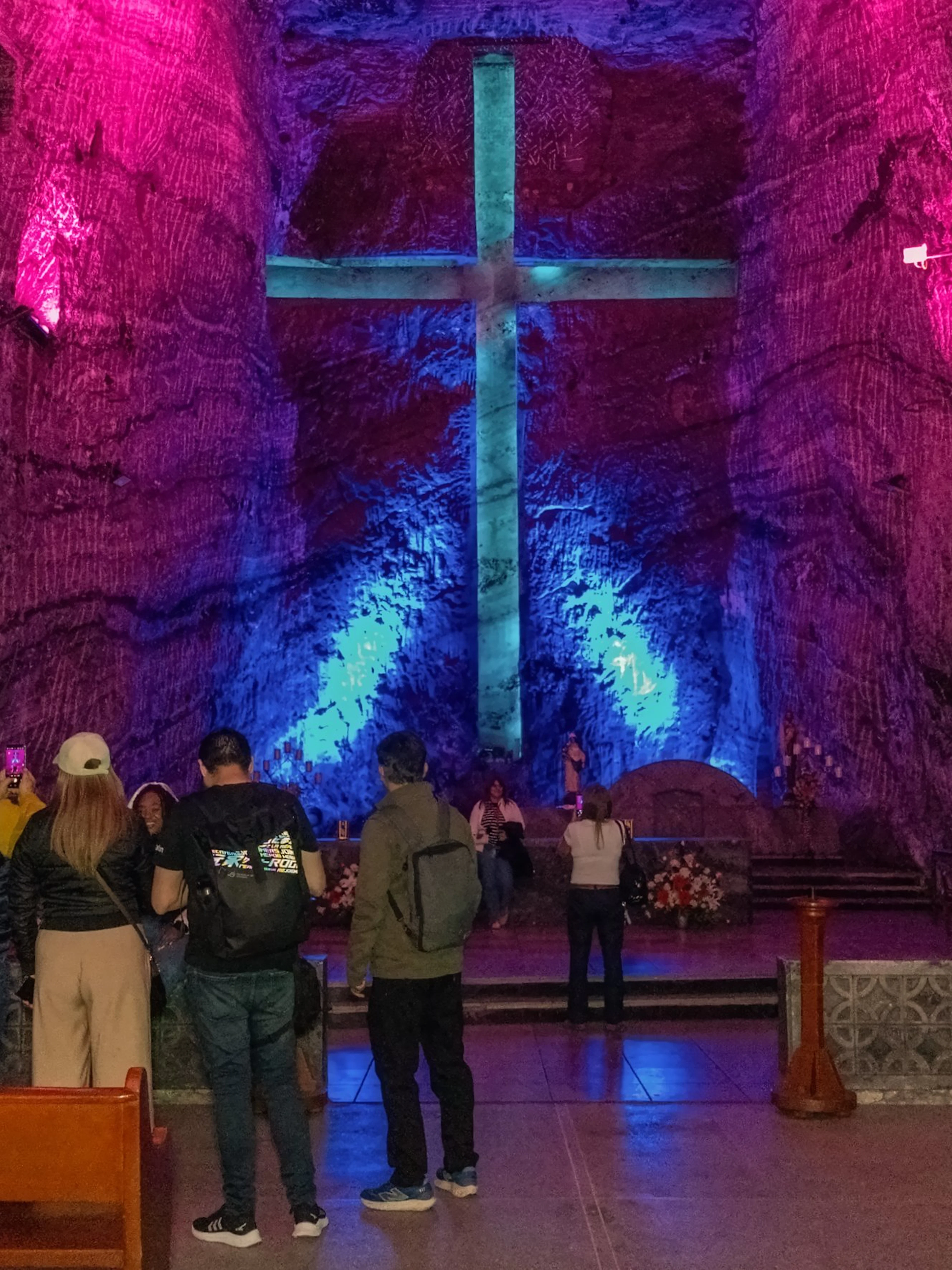 Tourists inside Zipaquira Salt Cathedral viewing illuminated cross.