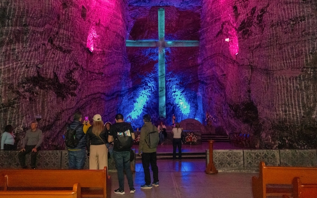 Tourists inside Zipaquira Salt Cathedral viewing illuminated cross.