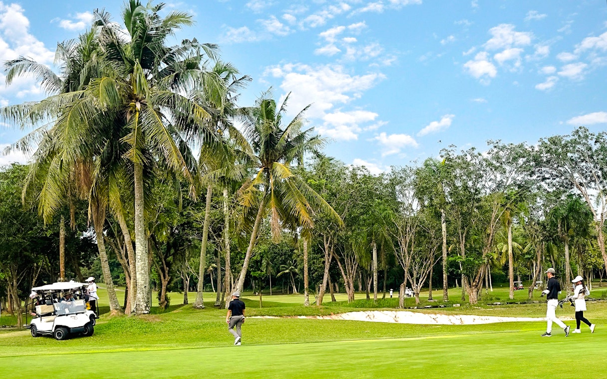 Golfers walking on the green at Batam Island Country Club golf course, surrounded by palm trees.