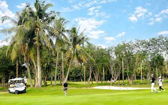 Golfers walking on the green at Batam Island Country Club golf course, surrounded by palm trees.