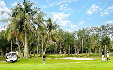Golfers walking on the green at Batam Island Country Club golf course, surrounded by palm trees.
