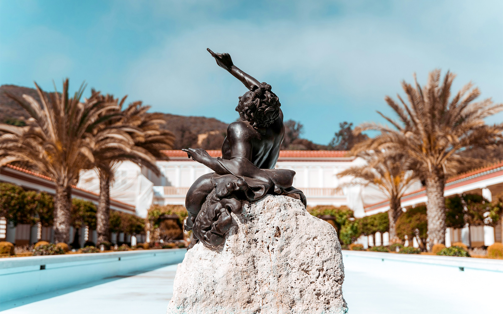 Statue in courtyard of Villa of the Papyri with palm trees and building in background.