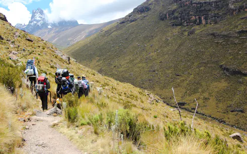 Hikers trekking on a trail with Mount Kenya in the background, lush landscape, Nairobi day tour.