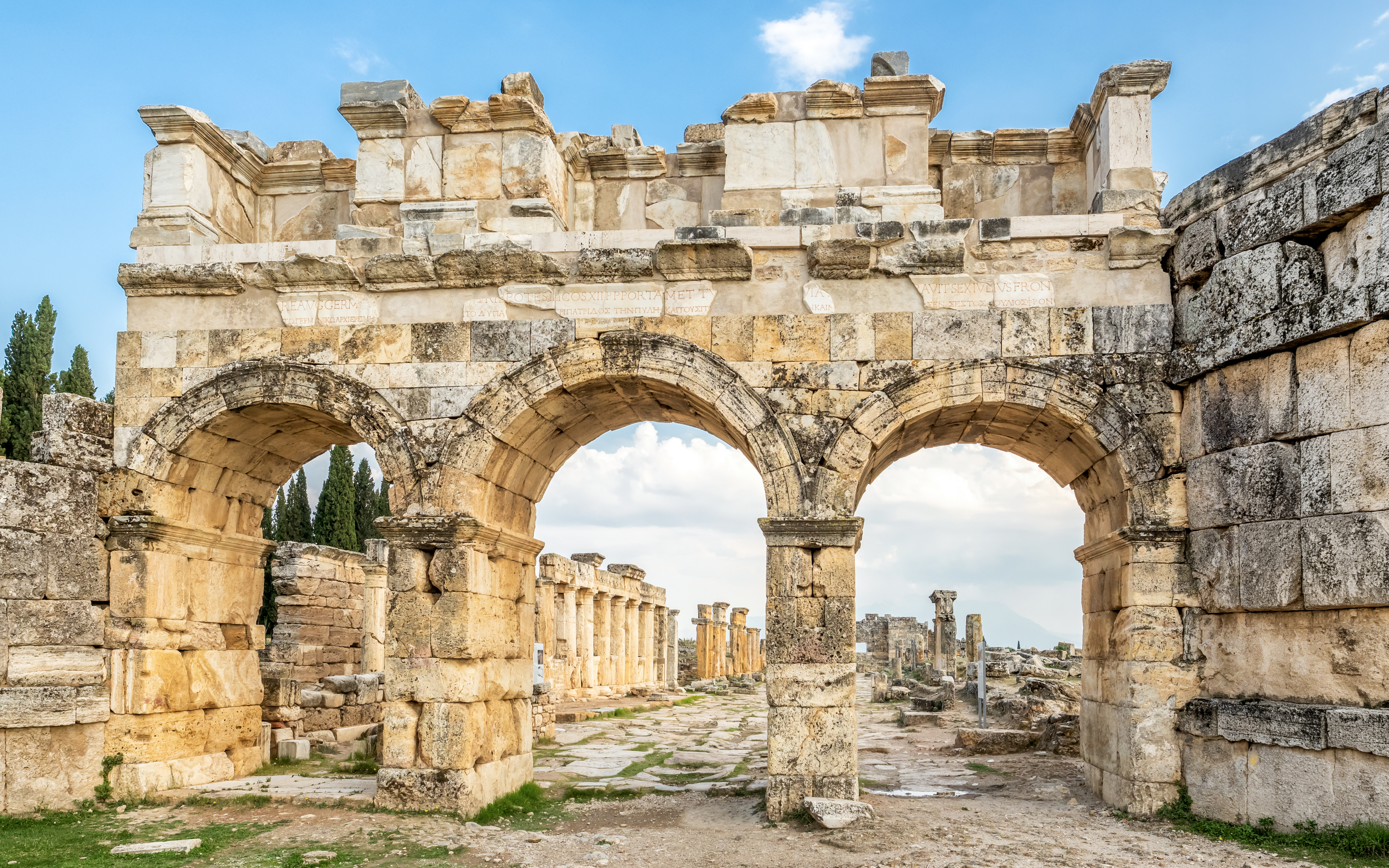 Facade of Domitian gates in ancient Hierapolis, Turkey, with stone arches and ruins in the background.