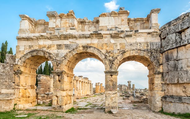 Facade of Domitian gates in ancient Hierapolis, Turkey, with stone arches and ruins in the background.