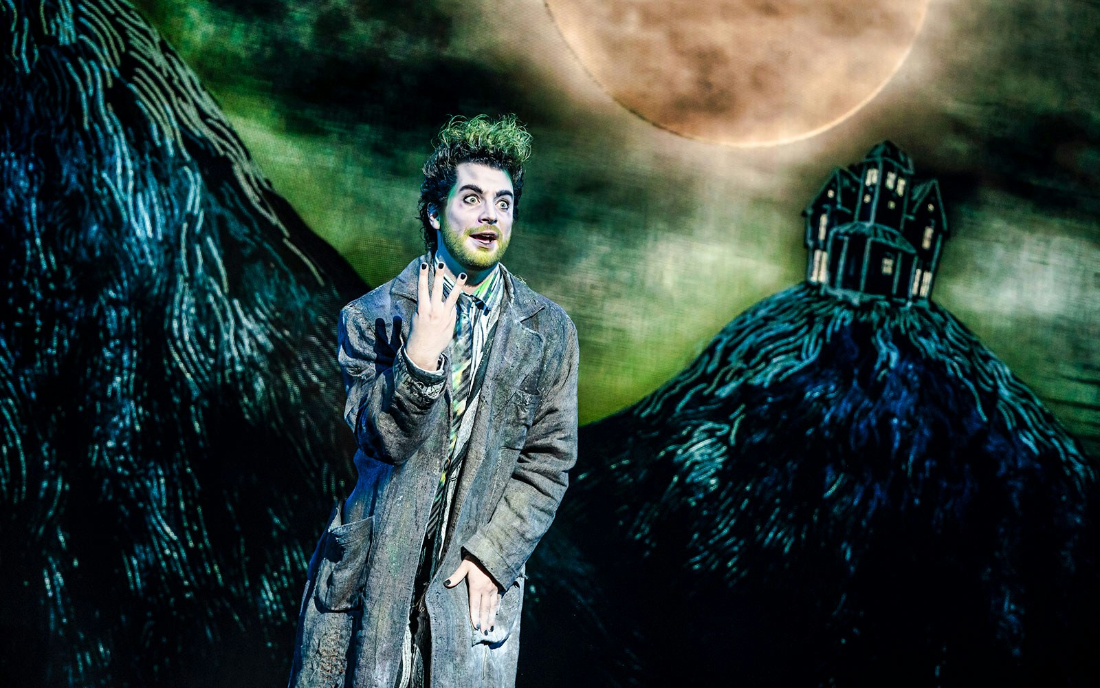 Performer in character at Beetlejuice Broadway show with eerie backdrop.