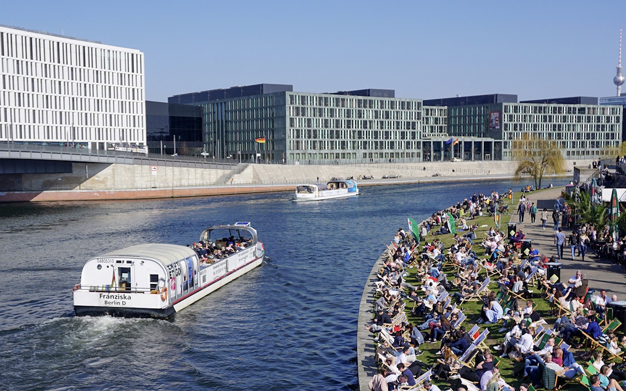 River cruise boat on Spree River in Berlin with passengers and riverside crowd.
