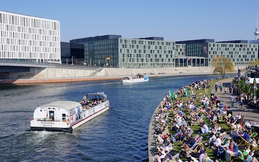 River cruise boat on Spree River in Berlin with passengers and riverside crowd.