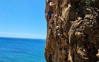 Rock climber scaling a cliff with ocean view in Cascais, Portugal, during guided tour.