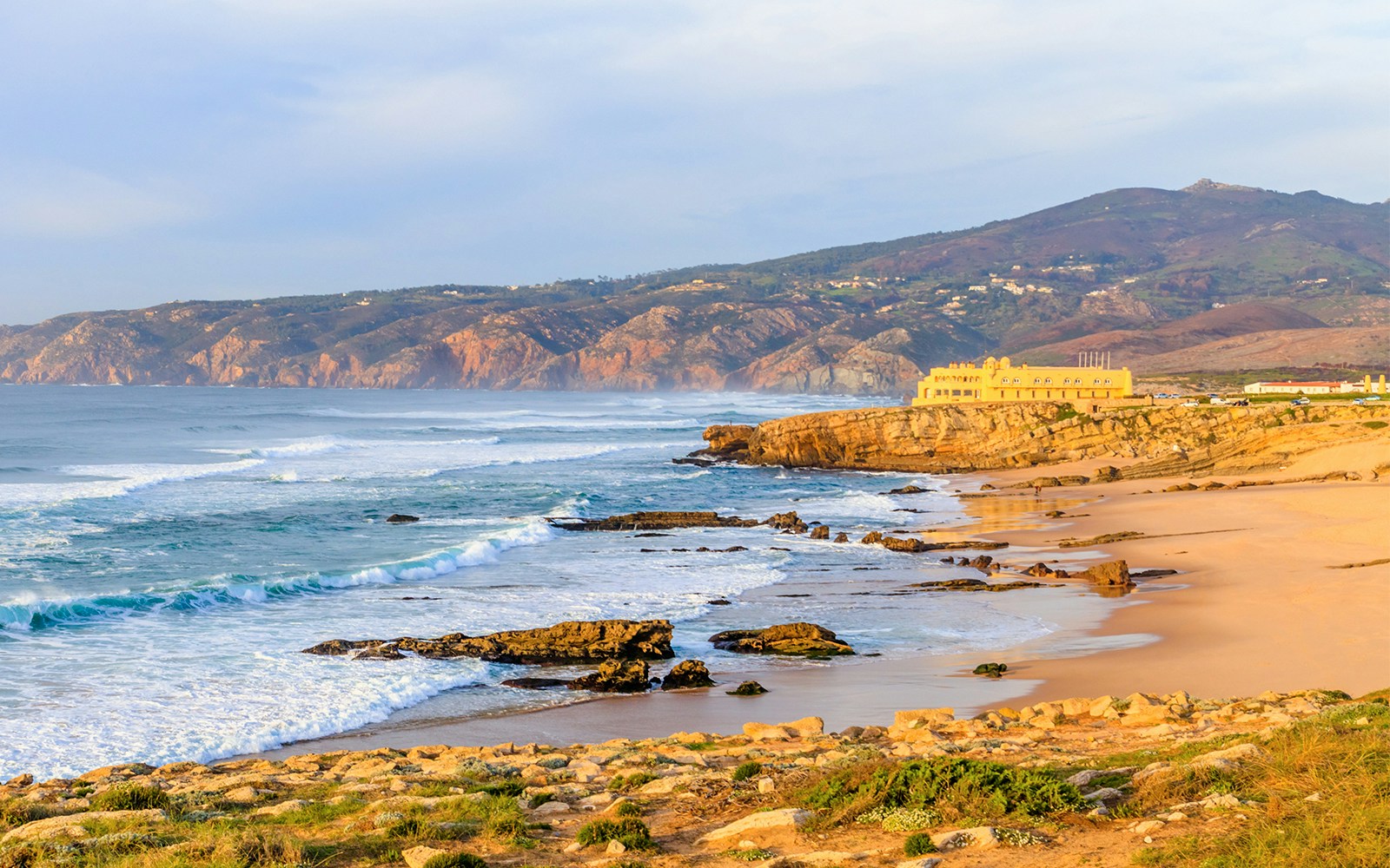 Panoramic view of Guincho Beach in Cascais with waves and rocky coastline.